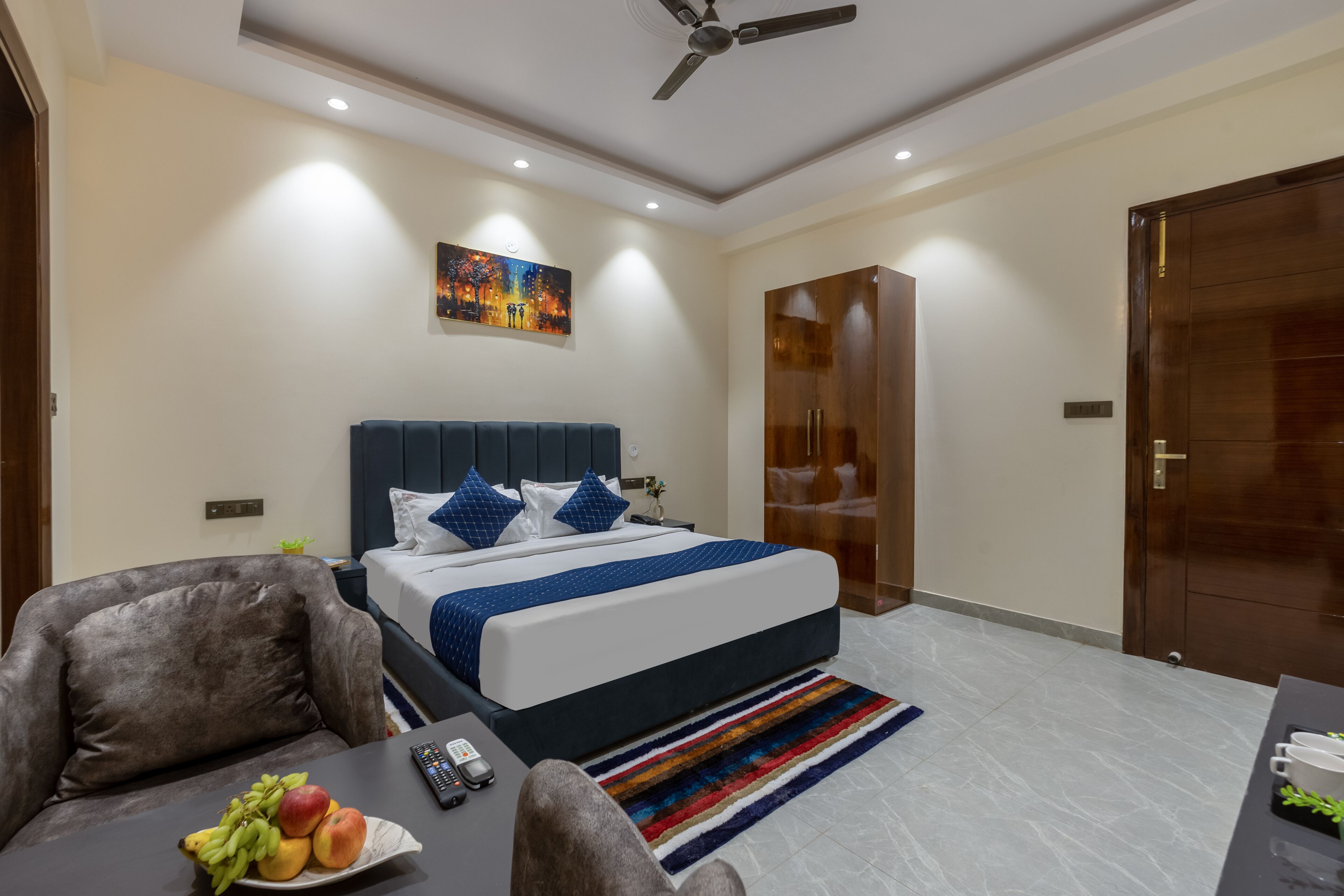 Una habitación de hotel moderna con una cama grande, un escritorio con frutero, un control remoto y un ventilador de techo.