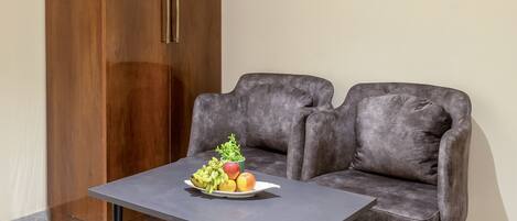 Quarto com uma mesa escura de cinza, duas cadeiras estofadas em cinza, um guarda-roupa de madeira com puxadores de latão e uma fruteira sobre a mesa.