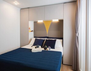 A modern bedroom with a bed, pillows, and a bedside table. - Mobilheim auf einem Campingplatz in Pietra Ligure (Pietra Ligure)