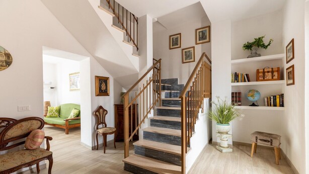 Una escalera con barandillas de madera, un sofá verde, un banco de madera y una estantería con libros y un globo terráqueo.