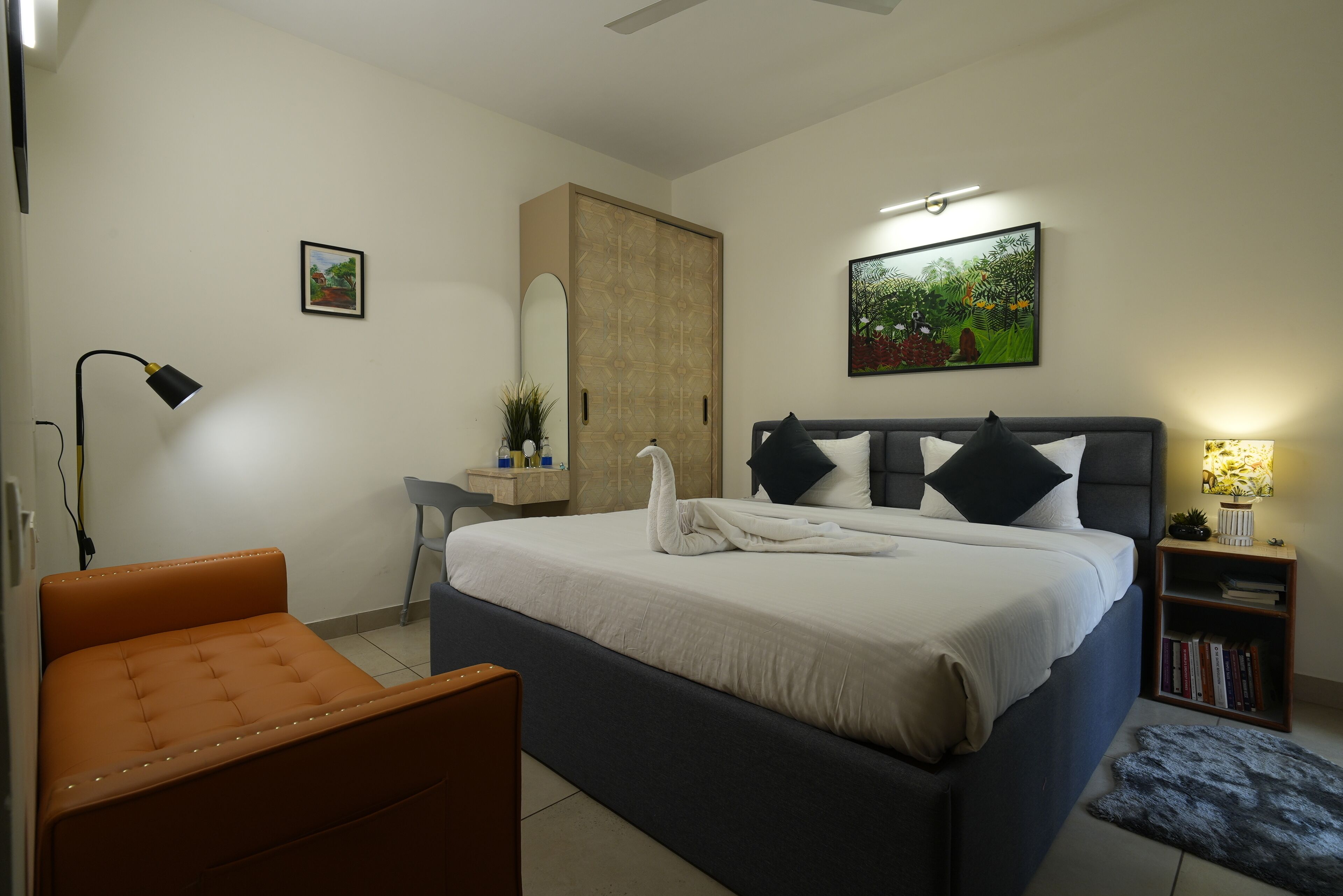 Un dormitorio con cama, escritorio, silla, estantería y lámpara de pared.