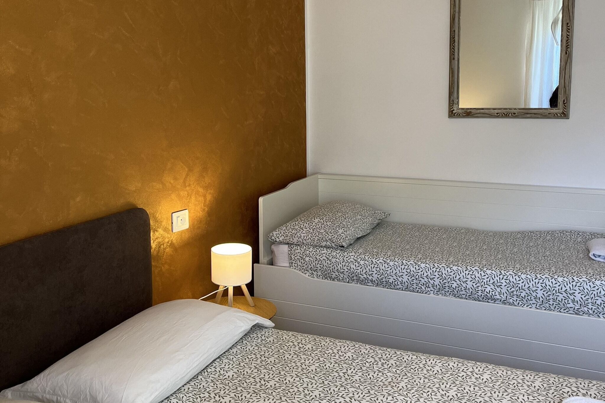 A hotel room with a bed, a bedside table with a lamp, a mirror, and a patterned bedspread.