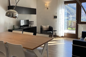 A modern kitchen with a dining area, a TV, and a view of a mountainous landscape. - Panoramic Lakefront Apartment for 5 (Pieve di Ledro)