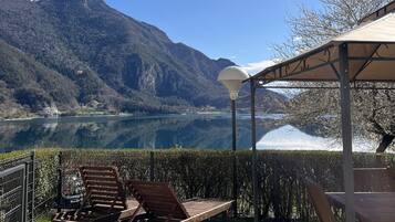 Eine Terrassenausrichtung am Seeufer mit einer Holzbank, einer Pergola mit einer Lampe und einem Berg im Hintergrund.