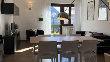 Ein modernes Wohnzimmer mit Esstisch, Stühlen, einer Couch, einem Fernseher und einem Fenster mit Blick auf Berge.