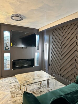 A modern living room with a fireplace, a flat-screen TV, and a herringbone-patterned wall. - Quaint, chic,   art nouveau 1- bedroom Garden apartment in East Brooklyn (Brooklyn)