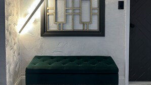 Una habitación con un banco tapizado en verde, un panel decorativo en la pared y un piso con estampado de espiga.