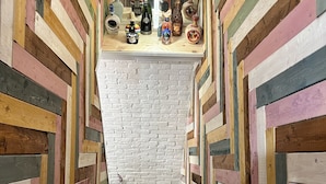 Una escalera estrecha con paneles de madera de colores en las paredes y una pared de ladrillo blanco al final.