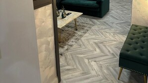 Una sala de estar moderna con piso de patrón espiga, un sofá verde, un otoman tapizado y un adorno de pared.