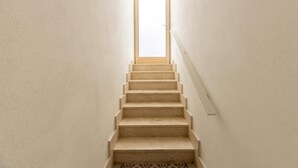 Eine schmale, mit Teppich belegte Treppe mit einem Holzhandlauf, die zu einem Dachfenster führt.