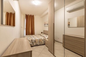 Un dormitorio con cama, mesita de noche, cómoda, espejo y aire acondicionado.