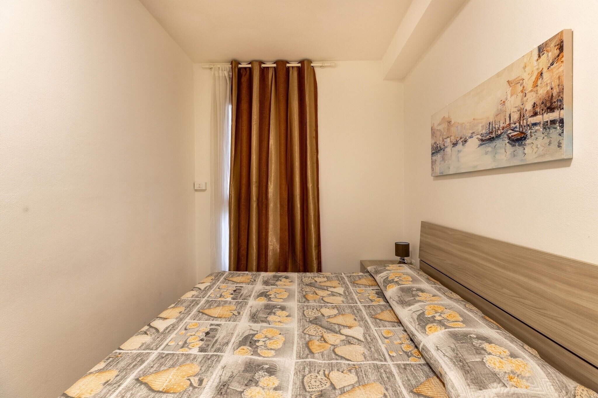 Une petite pièce avec un lit recouvert d’une courtepointe à motifs, un tableau accroché au mur et un rideau.