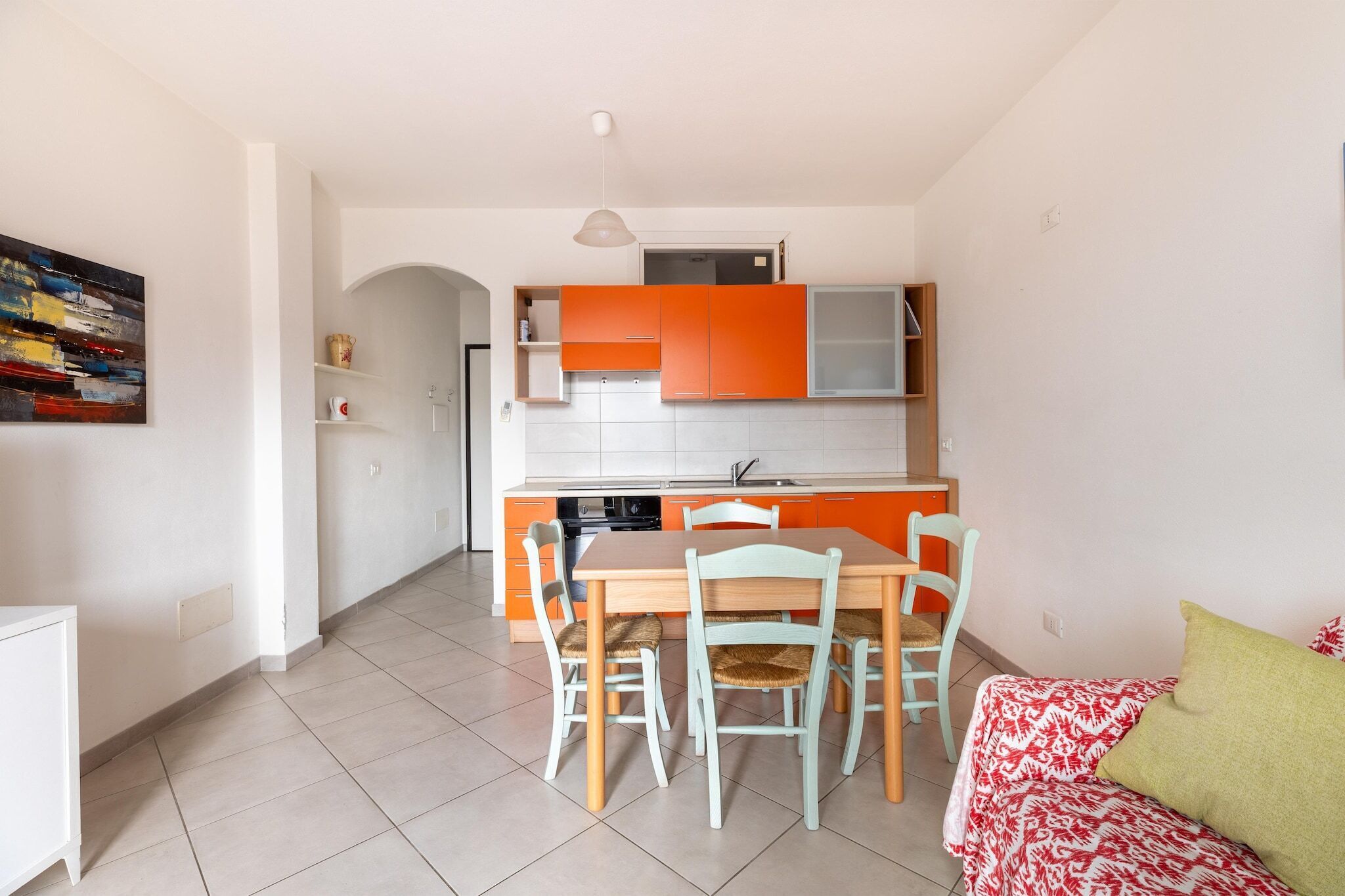 A modern kitchen with orange cabinets, a dining table with chairs, and a sofa in a living area.