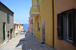 Una calle estrecha flanqueada por edificios, cielo despejado y un coche estacionado a lo lejos.