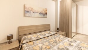 Ein Schlafzimmer mit Bett, Nachttisch, Lampe, einem Bild an der Wand und einem Kleiderschrank.