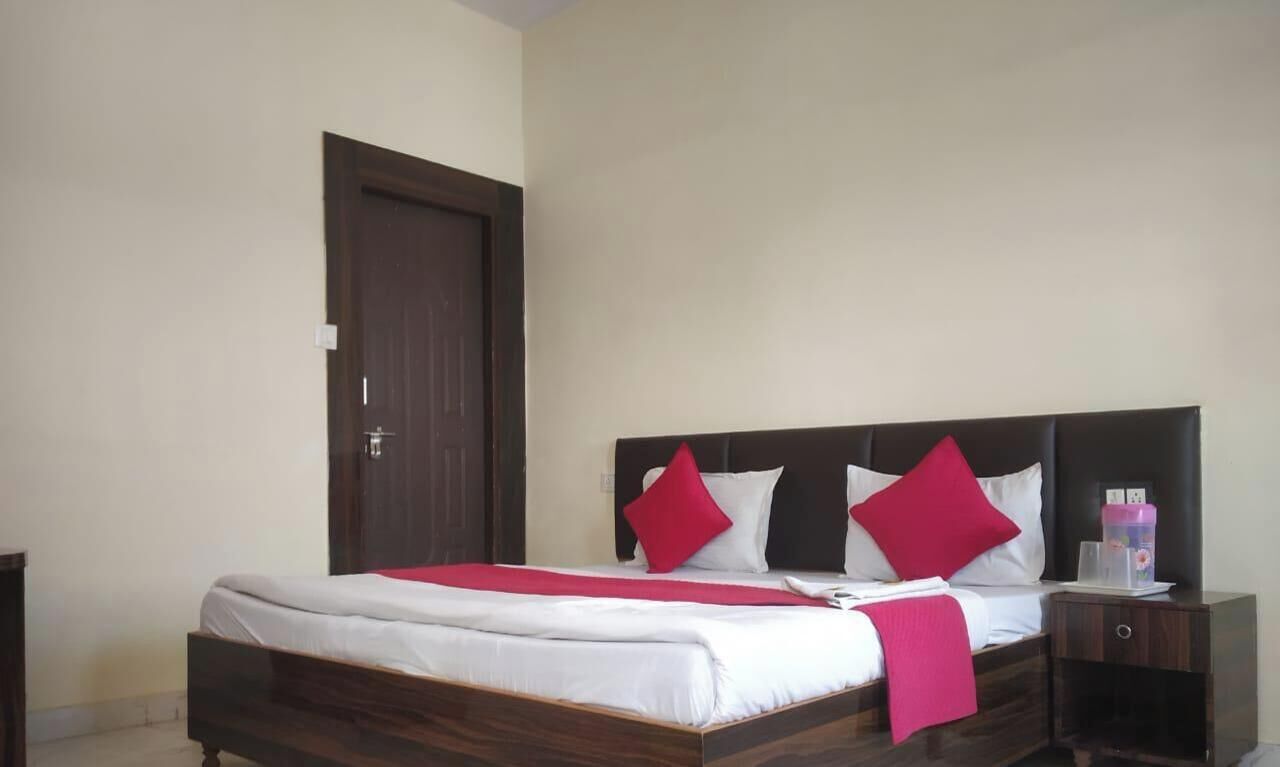 A neatly made bed with white bedding and red pillows, a wooden headboard, a nightstand with a lamp, and a closed door.