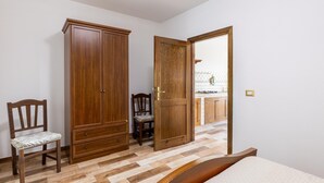 Ein Schlafzimmer mit Holzschrank, einem Sessel, einem Bett und einer offenen Tür, die auf einen Balkon führt.
