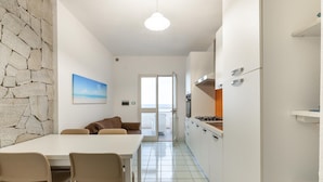 A kitchen with a dining area, a stone wall, and a view through a glass door. - Beachfront terrace and air conditioning (Castelsardo)