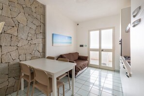 A room with a stone wall, a painting, a sofa, a dining table with chairs, and a kitchen area.
