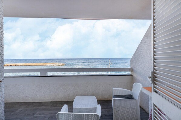 A balcony with white wicker furniture, a view of the sea, and a concrete barrier.