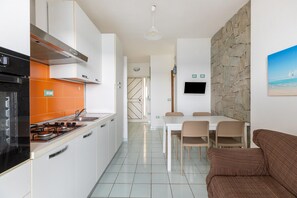Een moderne keuken met witte kasten, een oranje achterwand en een eethoek met een stenen muur en een schilderij van een strand.