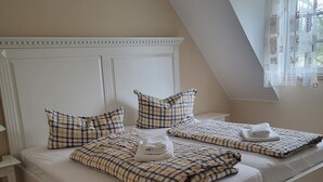 A double bed with a checkered bedspread and pillows, a small bedside table, and a window with curtains. - Welcome to our Gala vacation apartment (Stade)