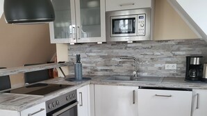 A modern kitchen with white cabinets, a built-in oven, a microwave, and a large black pendant light. - Welcome to our Gala vacation apartment (Stade)