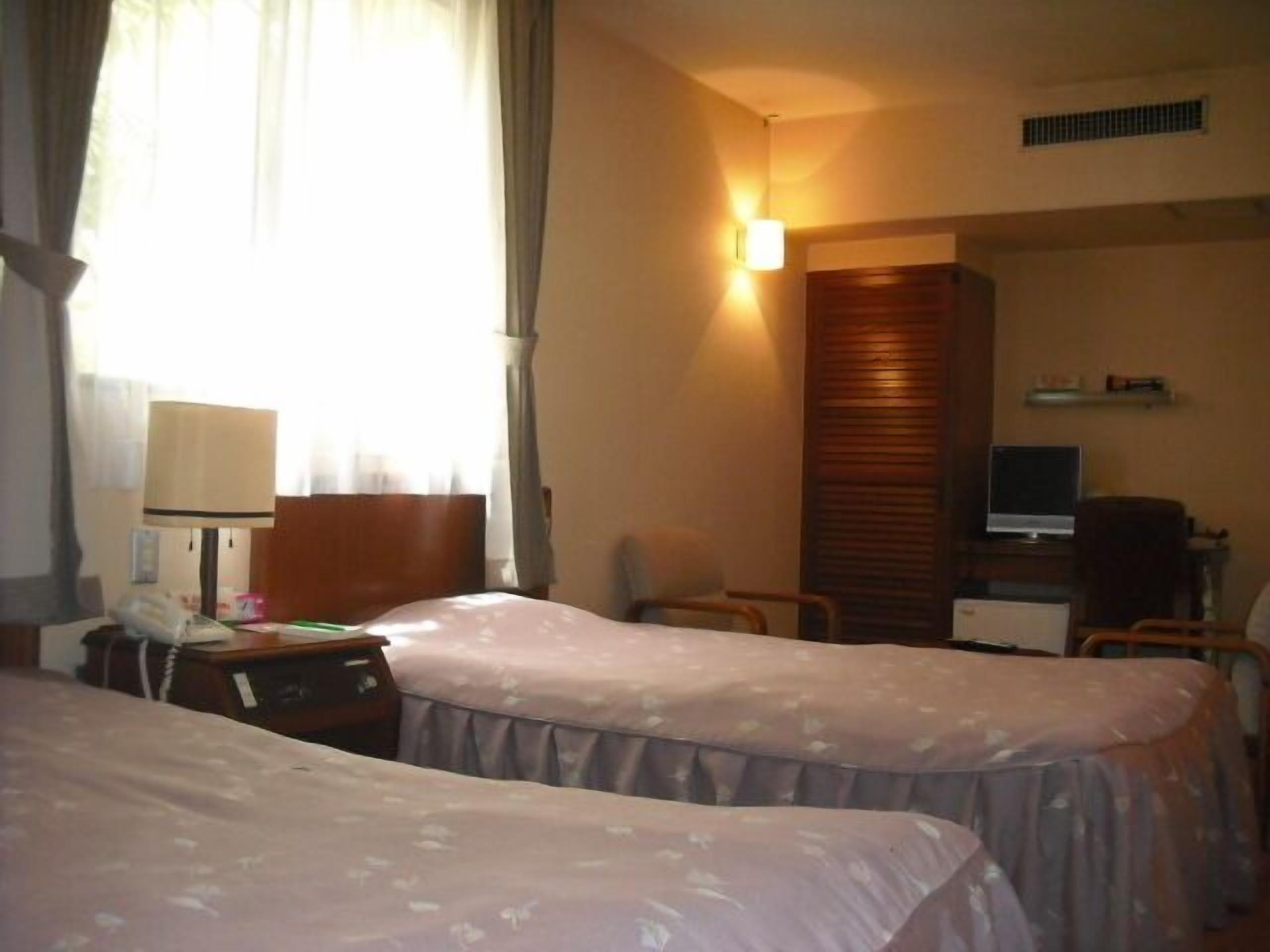 Une chambre d’hôtel avec deux lits, un bureau équipé d’un ordinateur, une chaise et une lampe.