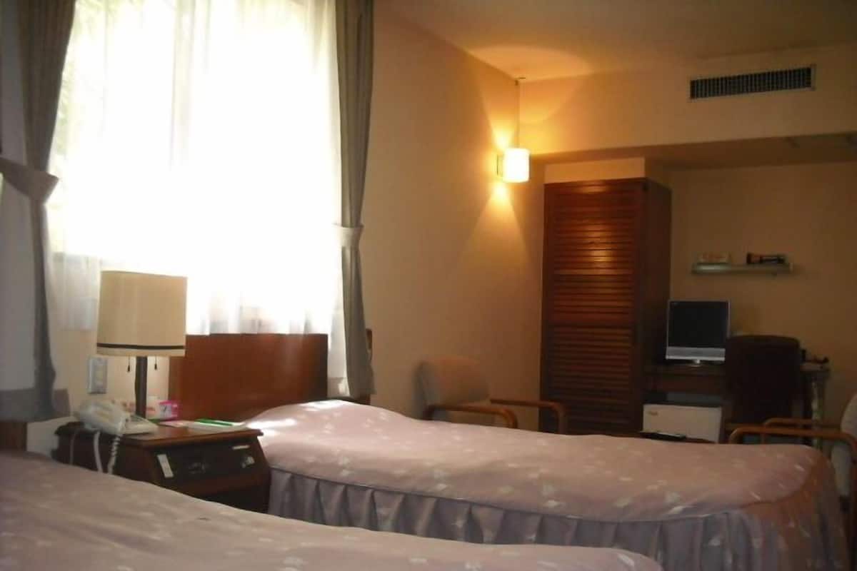A hotel room with two beds, a desk with a computer, a chair, and a lamp.
