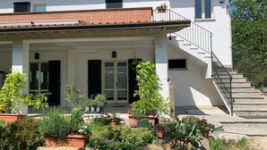 Une maison à deux étages dotée d’un porche couvert, d’un escalier et de diverses plantes en pot.