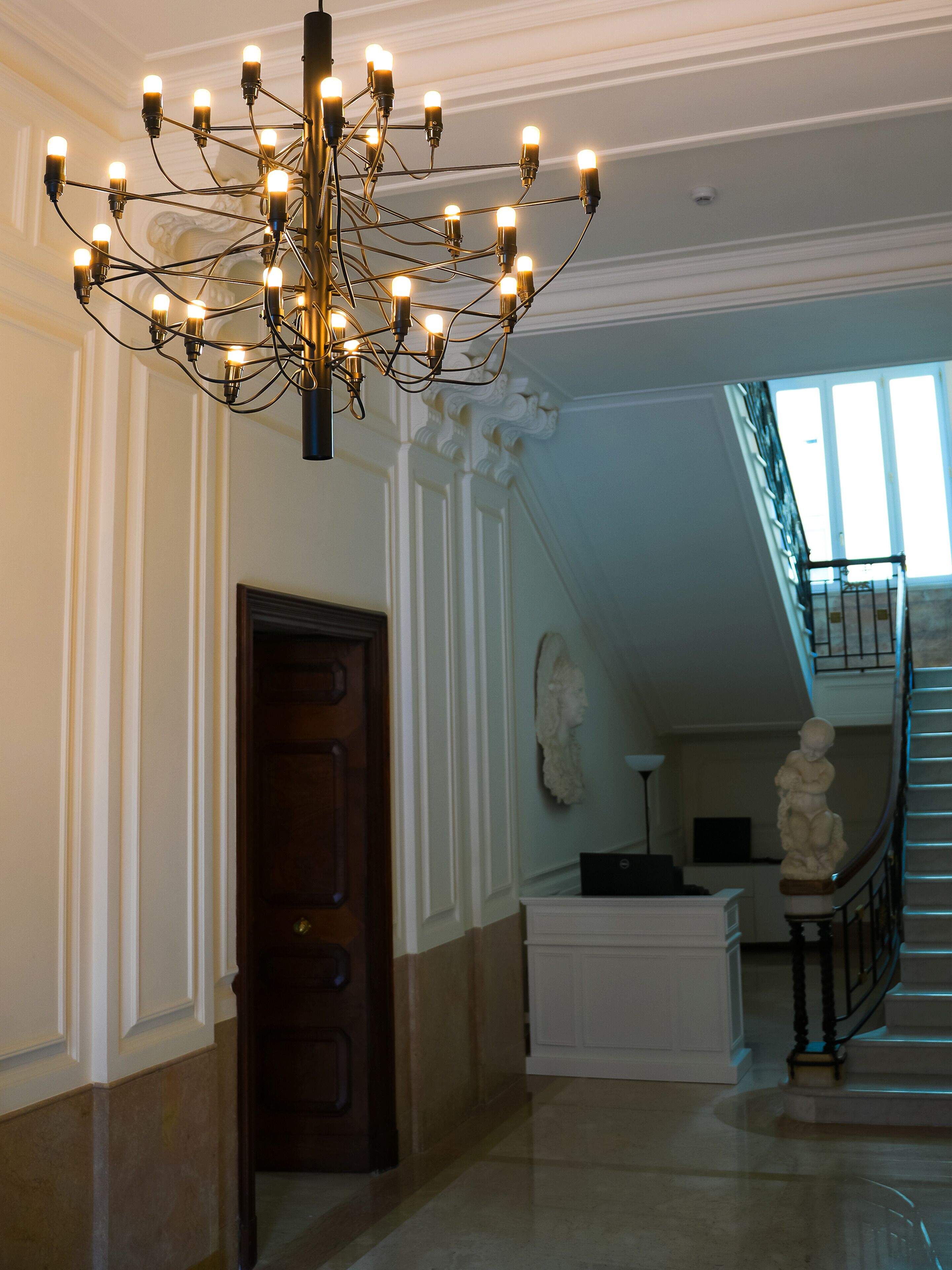 Un vestíbul majestuós amb un lampadari, una escala i una estàtua.
