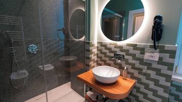 A modern bathroom with a glass shower enclosure, a wooden vanity with a white sink, and a round mirror with a built-in phone.