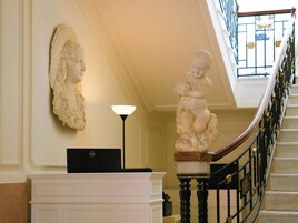 Una escalera con barandilla de mármol, una escultura en la pared y un escritorio con una computadora portátil.