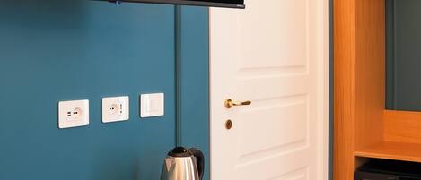 A room with a wooden desk, a chair, a television mounted on the wall, and a door with a coat rack.