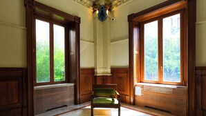 A room with a green chair, wooden paneling, large windows, and a marble floor. - Villa Liberty (Castellammare di Stabia)