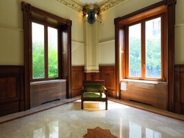 Una habitación con una silla verde, paneles de madera, ventanas grandes y piso de mármol.