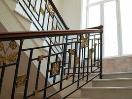 Una escalera con barandales de metal negro ornamentado y baranda de madera.