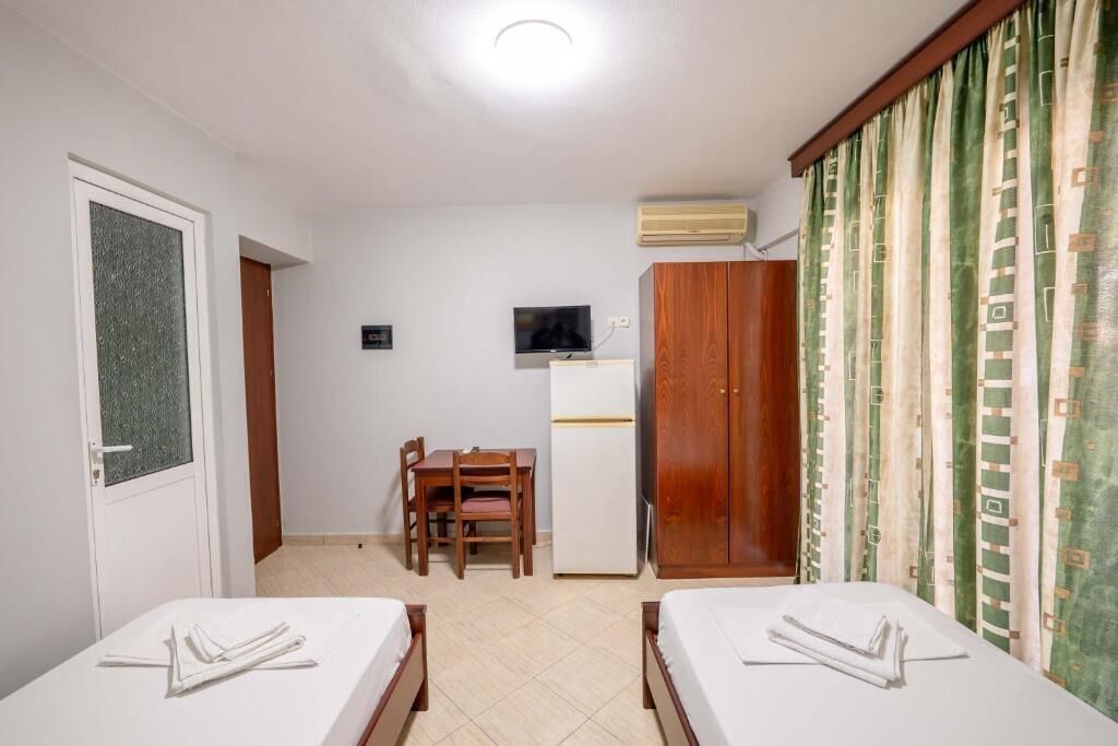 A room with two beds, a desk, a chair, a television, and an air conditioning unit.
