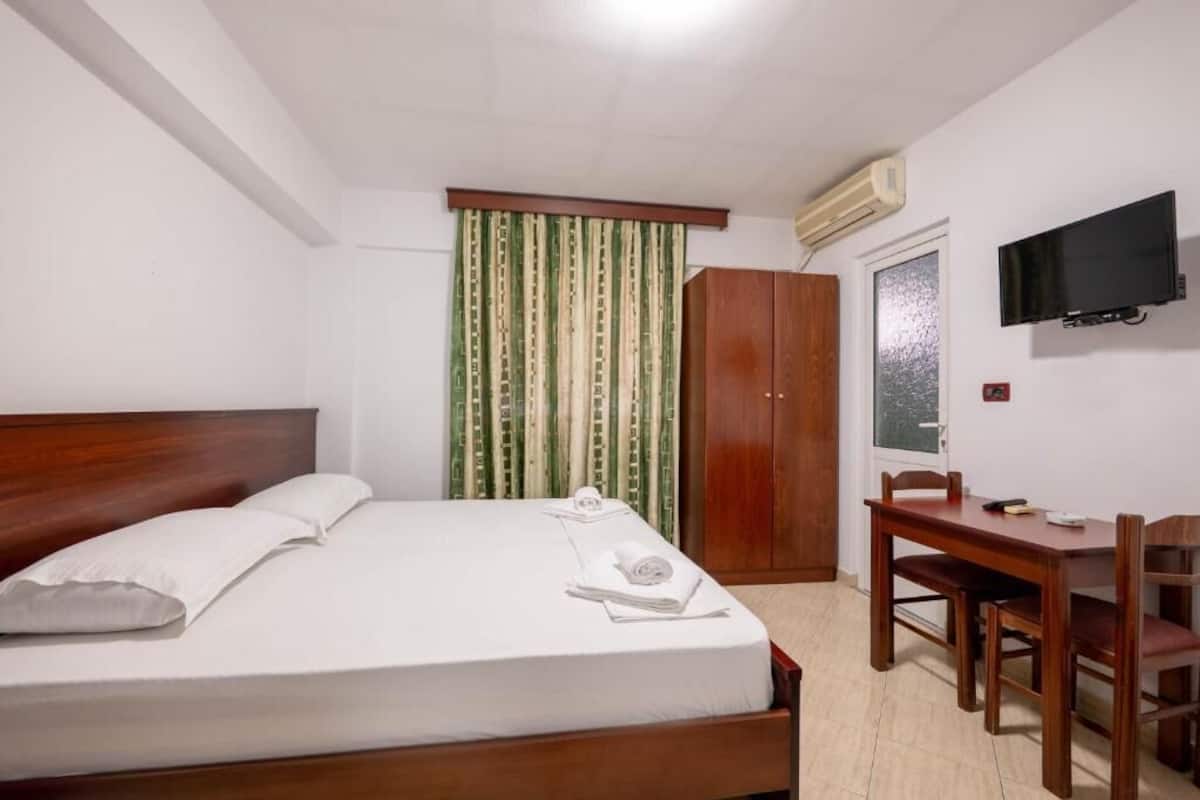 A hotel room with a bed, a desk, a chair, a wardrobe, a television, and a window with curtains.