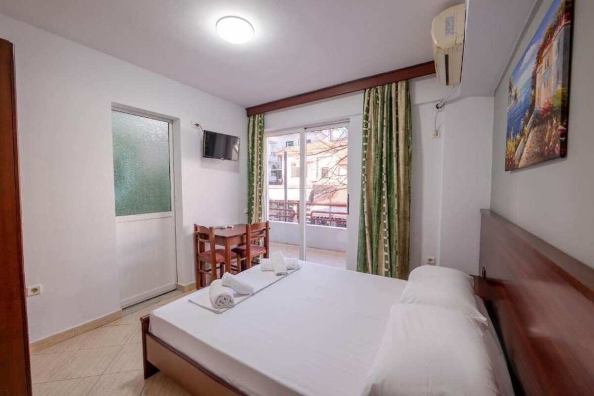 A hotel room with a bed, a TV, a desk with chairs, and a view through a glass door.