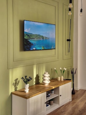 Ein Wohnzimmer mit einem an einer grünen Wand montierten Fernseher, einem Holzkonsolentisch mit Dekoration und einer modernen Leuchte.
