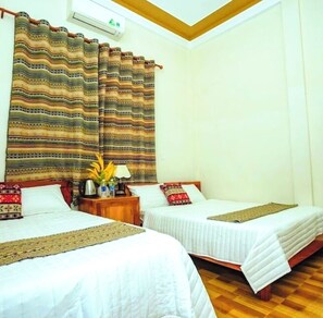 A hotel room with two beds, a wooden floor, a nightstand with a lamp, and a patterned curtain. - Family homestay  (Bo Trach)
