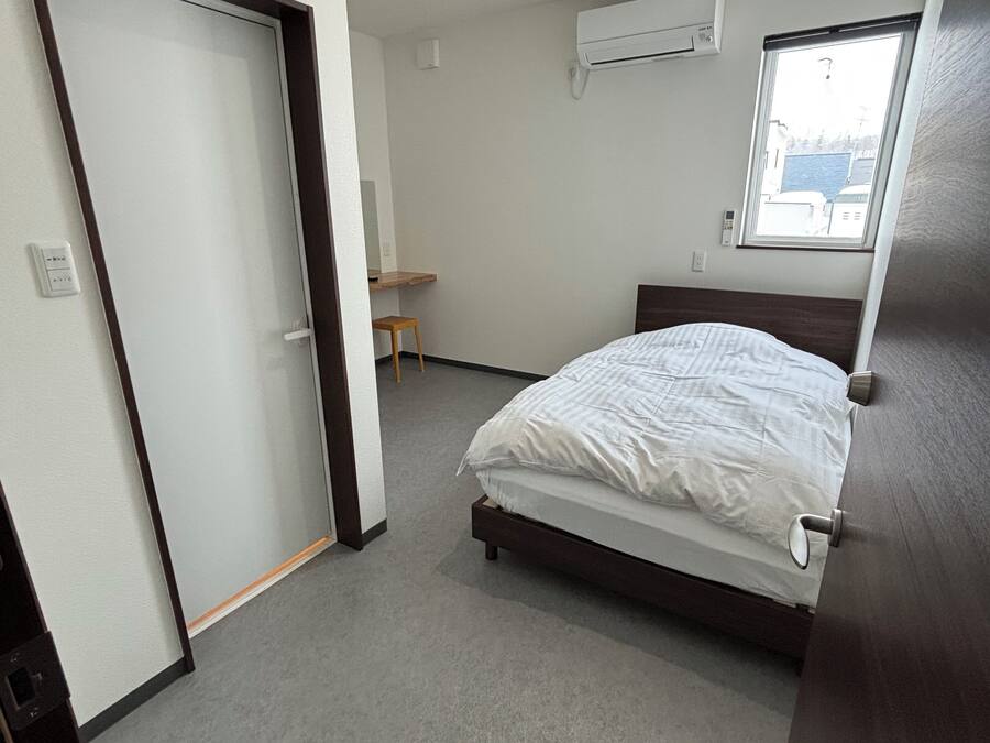 A bedroom with a bed, a window, an air conditioning unit, and a door.