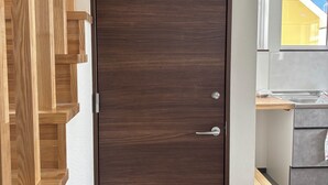 A dark wooden door with a silver handle and a keyhole, adjacent to a wooden staircase and a kitchen area with a countertop and cabinets.