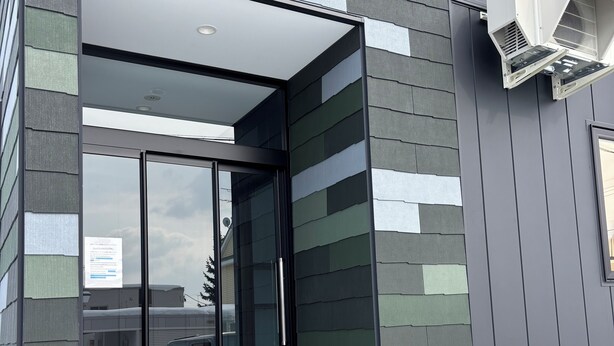 A modern building with a glass entrance, steps leading up to the door, and an air conditioning unit mounted on the exterior wall.