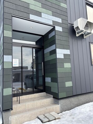 Un bâtiment moderne doté d’une entrée en verre, de marches menant à la porte et d’un appareil de climatisation fixé au mur extérieur.