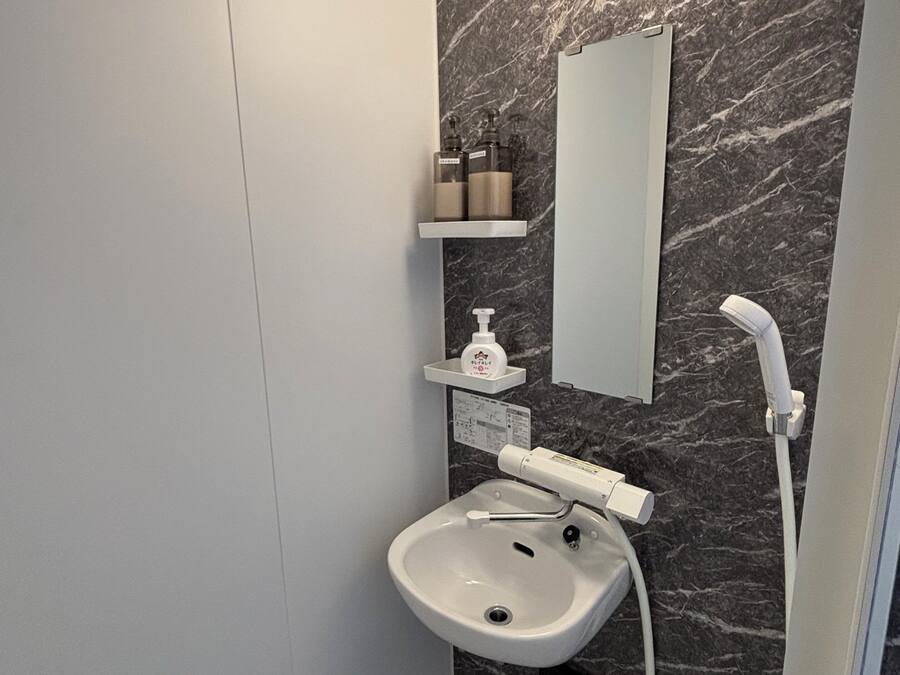 Un baño moderno con pared de mármol, lavamanos blanco, espejo y ducha.