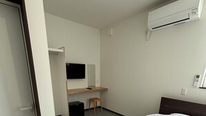 A hotel room with a bed, a desk, a chair, and an air conditioning unit.