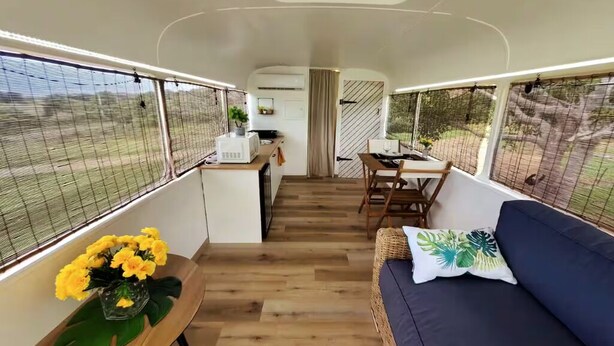 A compact RV interior with a kitchenette, dining area, and seating space. - Cozy 1-bedroom Caravan In Bourail with AC (Bourail)
