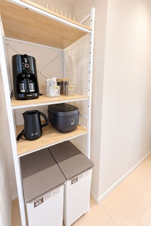 Eine Küchenzeile mit Kaffeemaschine, Wasserkocher, Slow Cooker und Vorratsgläsern auf Regalen.